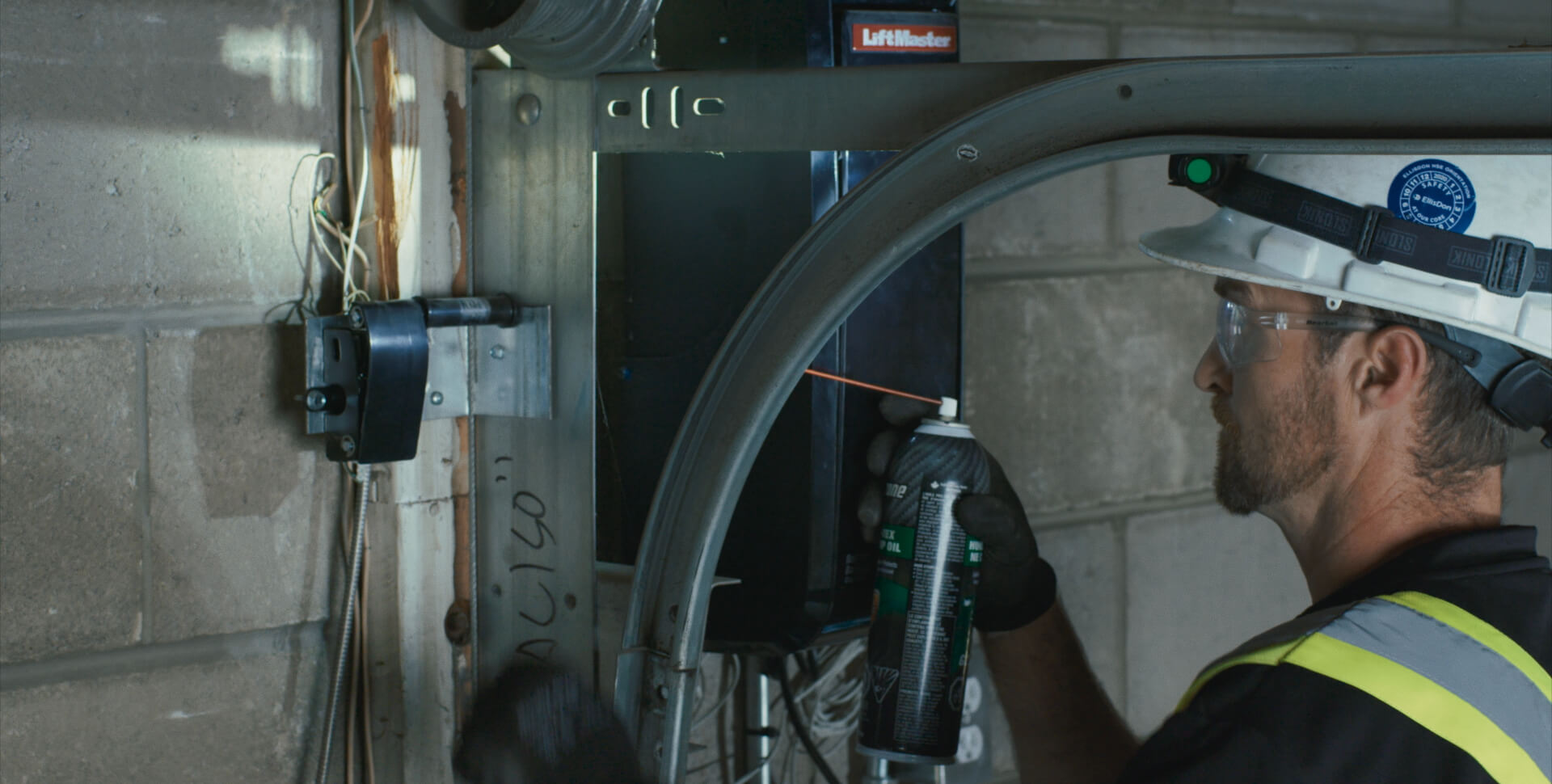 Wilcox technician lubricating garage door opener components during maintenance service